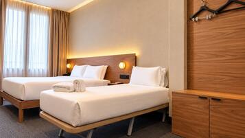 Habitación de hotel con dos camas, cabecera de madera, armario y perchero.