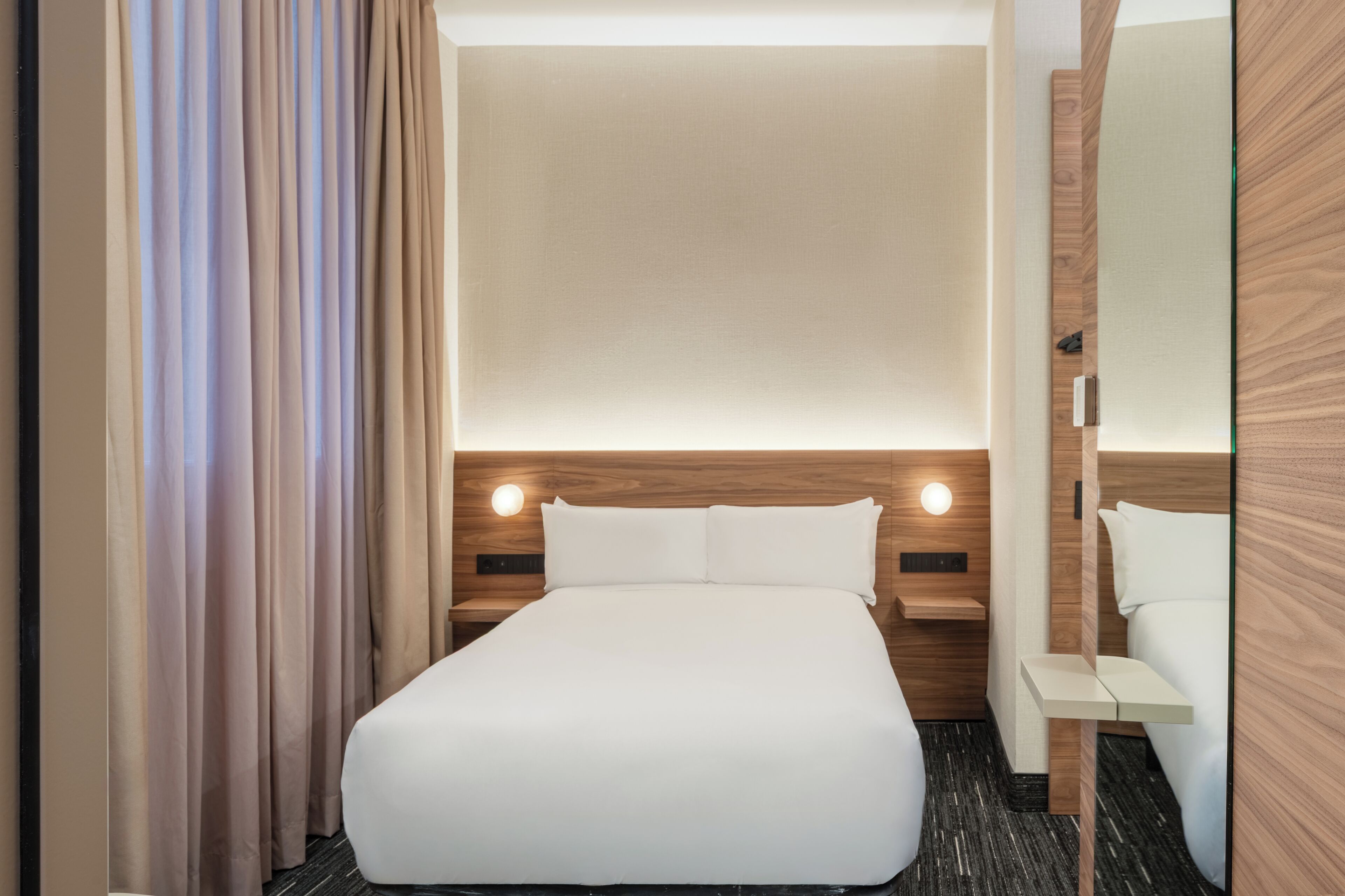 Una habitación de hotel con cama, mesitas de noche, cortinas y un espejo.