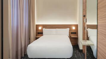 Una habitación de hotel con cama, mesitas de noche, cortinas y un espejo.