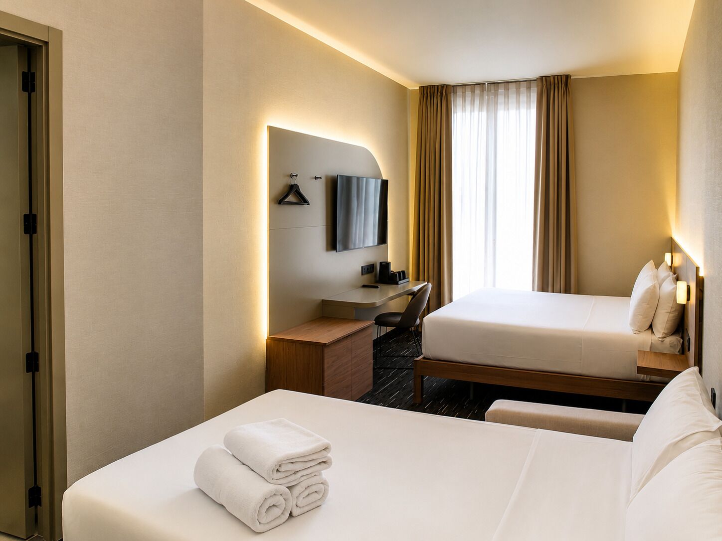 Een hotelkamer met twee bedden, een bureau, een stoel, een televisie en een deur naar de badkamer.