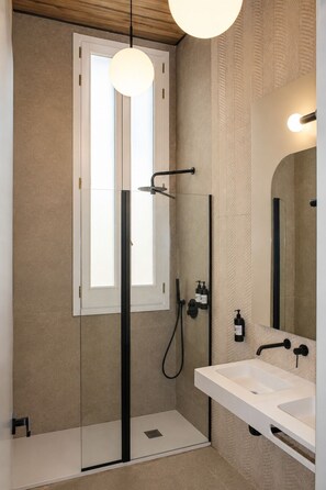 A modern bathroom with a glass-enclosed shower, a white sink, and a large mirror. - FORTINN Puerta del Sol (Madrid)