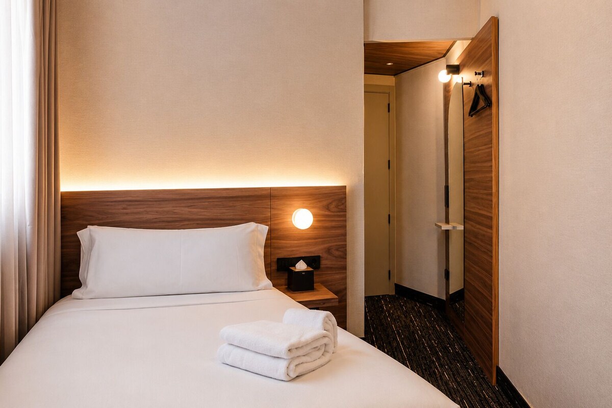 Een hotelkamer met een net opgemaakt bed, een bedlampje en een houten hoofdeinde.
