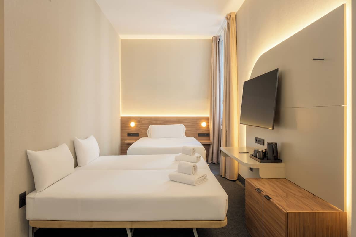 A hotel room with two beds, a TV, a wooden nightstand, and a built-in desk.