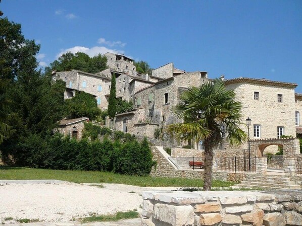 A stone building with multiple levels, surrounded by greenery and a clear sky.
