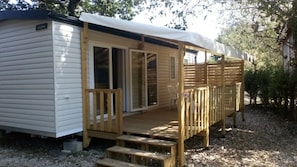 A mobile home with a wooden deck, sliding glass doors, and a covered porch.