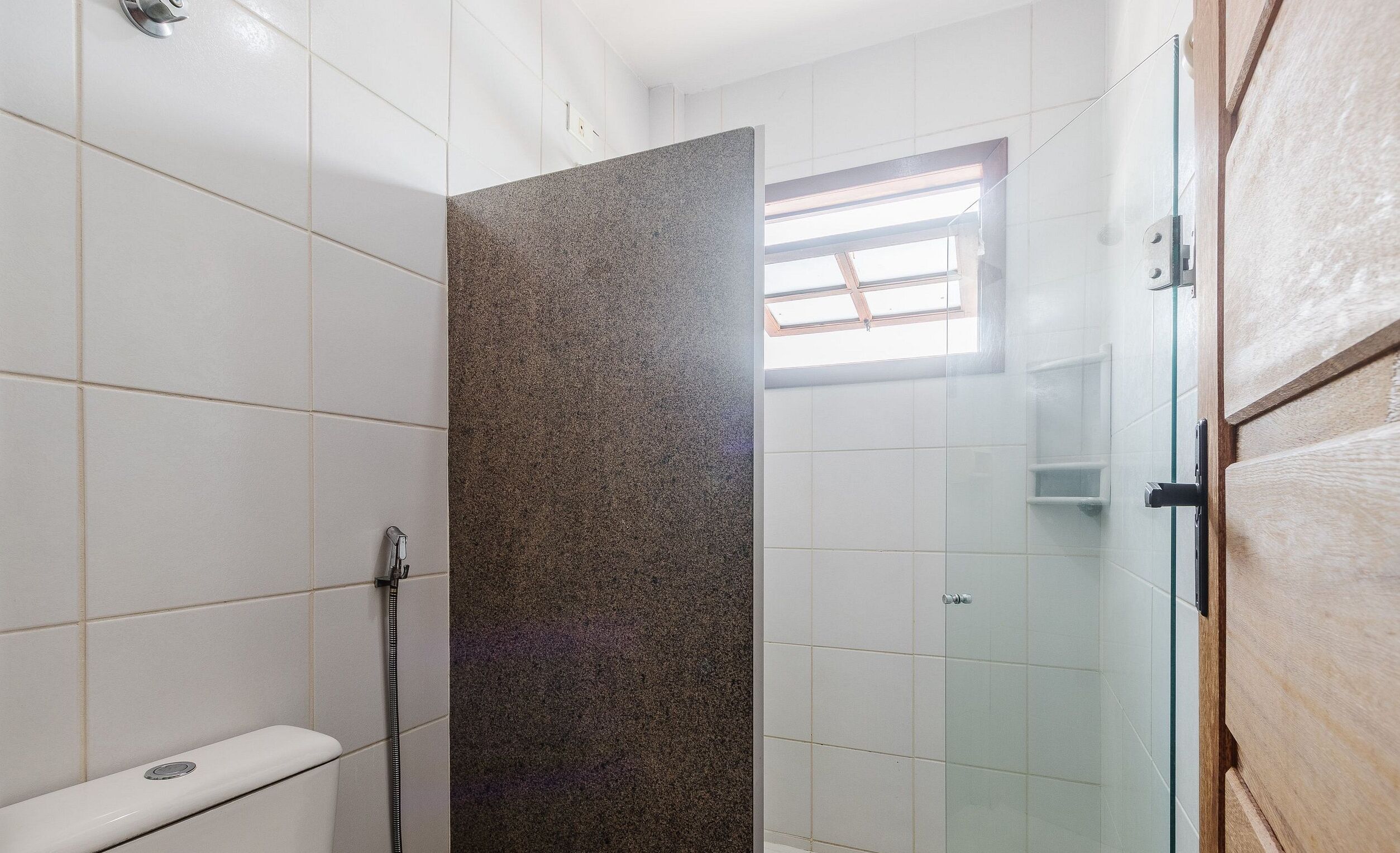 A shower with a glass door, a toilet, and a window in the shower area.