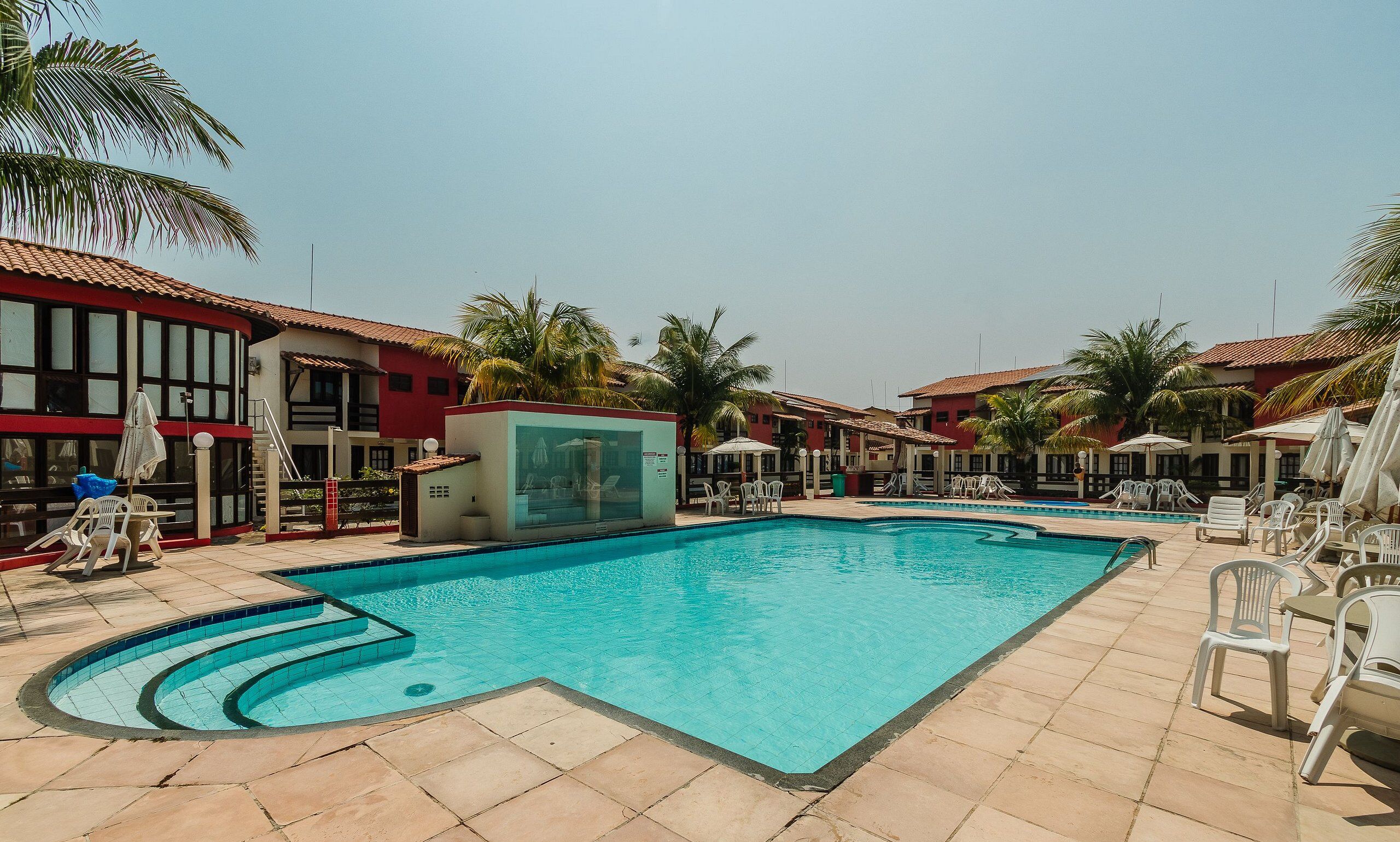 A swimming pool with lounge chairs and umbrellas, surrounded by buildings with red and white facades.