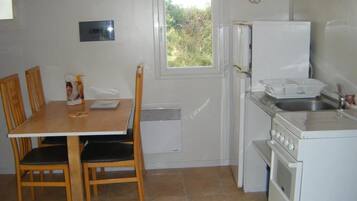 Une cuisine de taille réduite comprenant une table à manger, des chaises, un réfrigérateur, une cuisinière et une fenêtre.