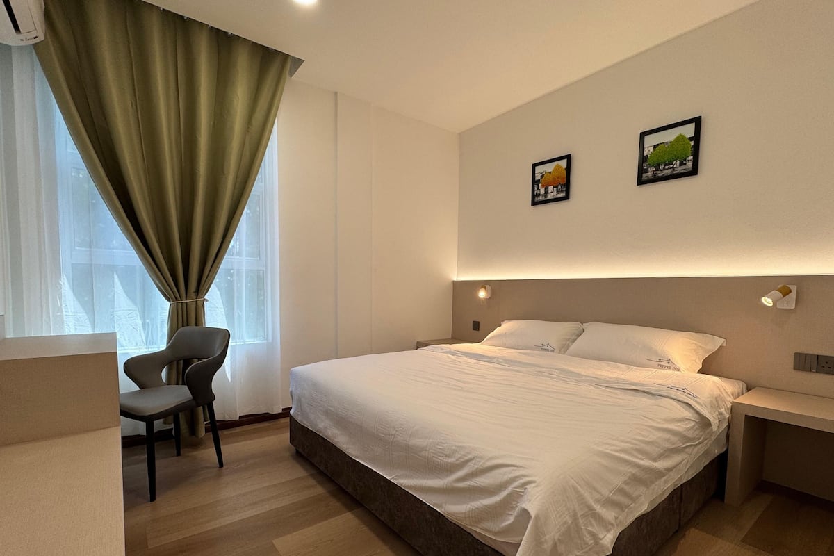 A modern hotel room with a large bed, a chair, a desk, and two framed pictures on the wall.