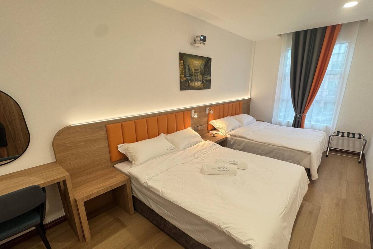A hotel room with two beds, a desk, and a mirror.
