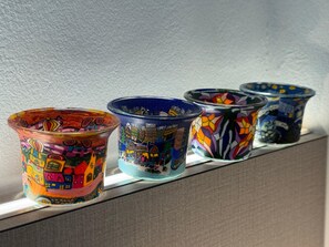 Four colorful ceramic containers with intricate designs, placed on a ledge against a textured wall. - Pepper Inn (Sibu)