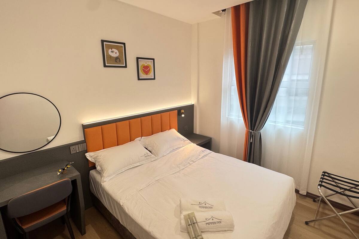 A hotel room with a bed, a desk, a chair, a mirror, and two framed pictures on the wall.