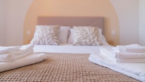 Een keurig opgemaakt bed met witte lakens en een textiel vloerkleed op de voorgrond.