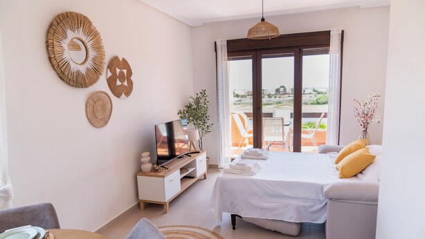 Een hotelkamer met een bed, een televisie, een eethoek met een gedekte tafel voor twee personen en een balkon met uitzicht.