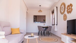 Een moderne woonkamer met een bank, eettafel, stoelen, een televisie en decoratieve wandkunst.