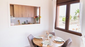 Een eetruimte met een ronde tafel voor vier personen, een houten kast erboven en een raam met gordijnen.
