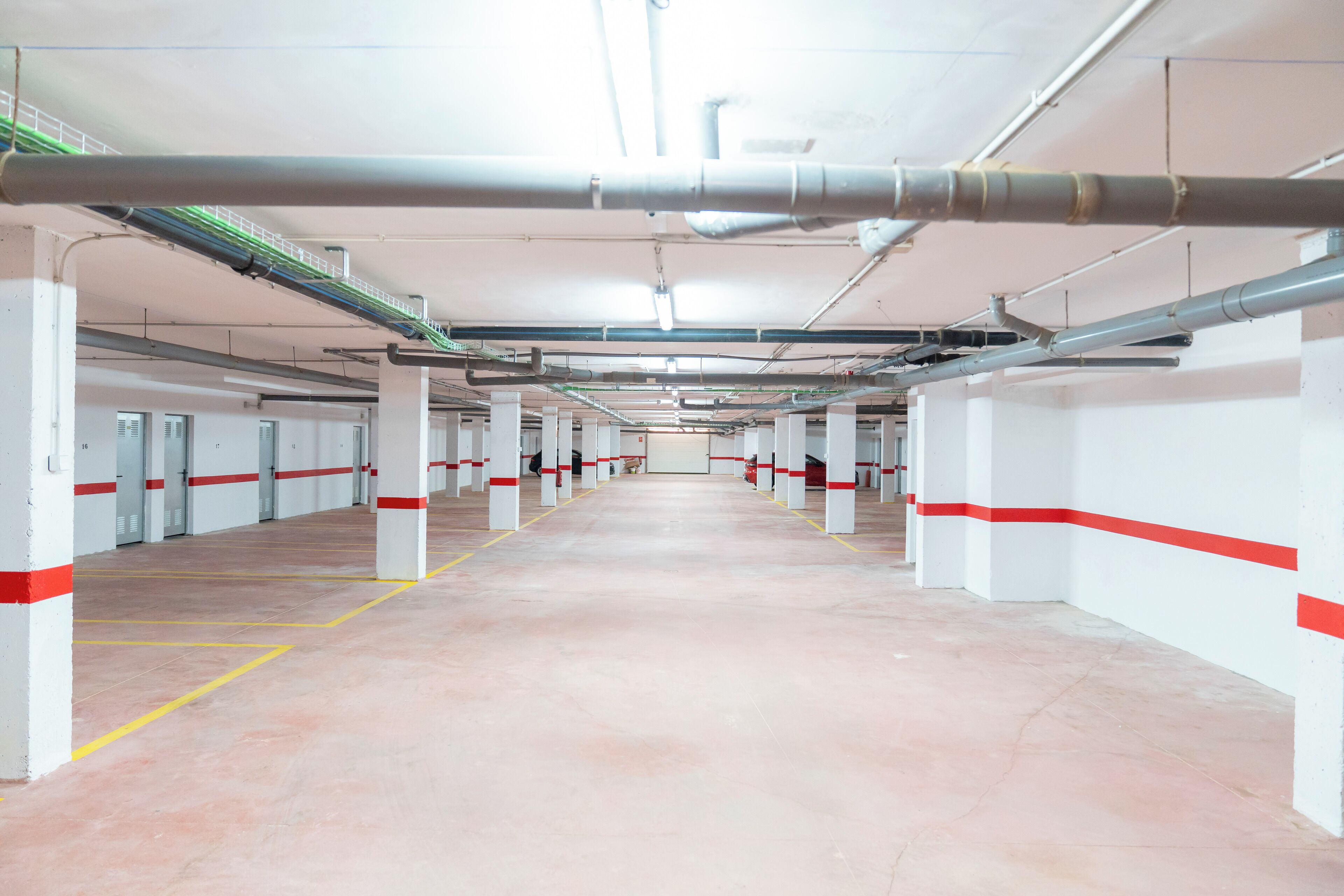 A clean, well-lit parking garage with white pillars and red stripes, featuring a clear path and multiple parking spaces.
