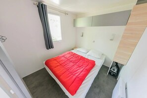 A small, modern bedroom with a bed, a window with curtains, a bedside table, and a built-in wardrobe.