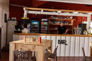 Un espace bar avec un comptoir en bois, des étagères remplies de bouteilles et un réfrigérateur.