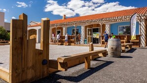 A rustic outdoor seating area with wooden benches and tables, a wooden fence, and a building with a tiled roof.