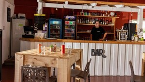 A bar area with a wooden counter, shelves stocked with bottles, and a refrigerator.