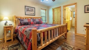 A bedroom with a wooden bed, a ceiling fan, a nightstand, and a door leading to another room. - *Amazing 2BD Cabin Near TOWN! Hot Tub + Fire Pit* (Sevierville)