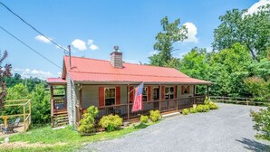 A two-story building with a red roof, a porch with a railing, and a flag. - *Amazing 2BD Cabin Near TOWN! Hot Tub + Fire Pit* (Sevierville)