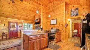 A wooden cabin interior with a kitchen featuring a granite countertop, wooden cabinets, a stove, and a refrigerator. - *Amazing 2BD Cabin Near TOWN! Hot Tub + Fire Pit* (Sevierville)