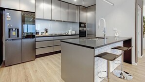 A modern kitchen with stainless steel appliances, a central island with bar stools, and a large window providing natural light.