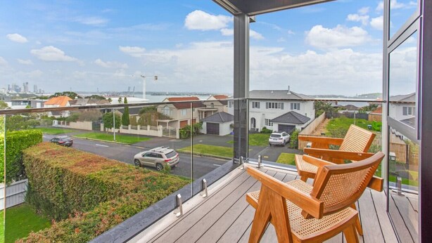 A balcony with wooden chairs, a view of a residential area, and a clear sky.