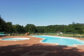 Piscina com deck de tijolos, cercada por árvores e uma área murada.