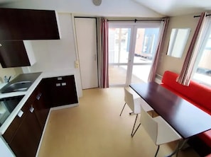 Cozinha compacta com pia, área de refeições com sofá vermelho e porta de vidro deslizante para área externa.