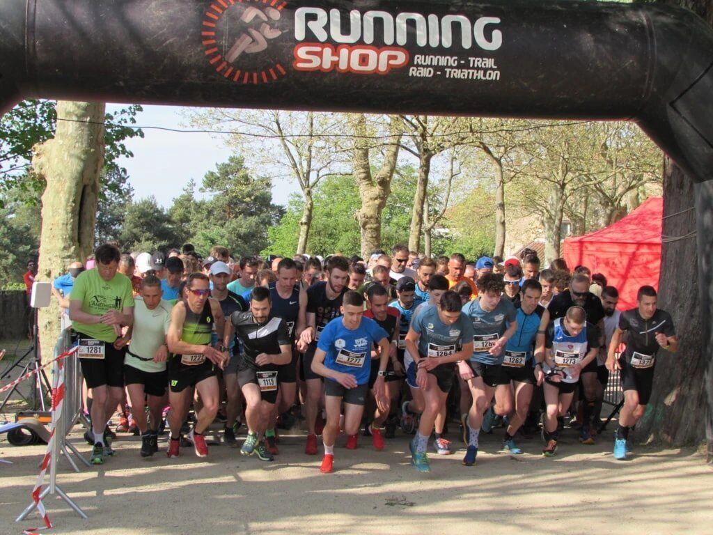 A group of runners at a starting line with a banner reading "RUNNING SHOP."