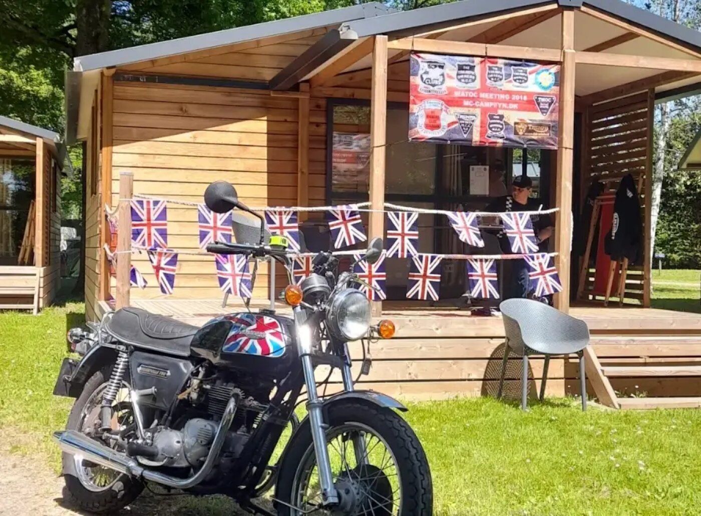 Une moto est garée devant un bâtiment en bois dont l’entrée est décorée d’un drapeau.