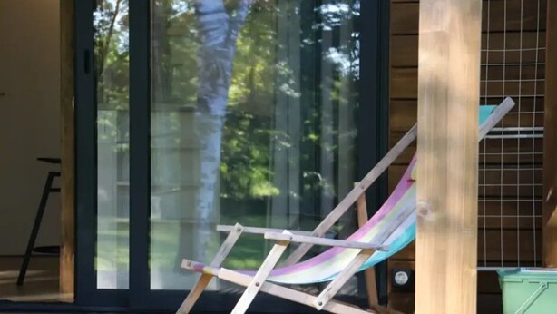Un pontile in legno con una comoda sedia lounge colorata, un cestino verde e una scala appoggiata al muro.