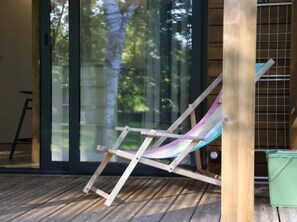 A wooden deck with a single colorful lounge chair, a green trash bin, and a ladder leaning against the wall. - ZEcamping 3* piscine animaux acceptés fitness tente 35m2 7 pers (Sauxillanges)
