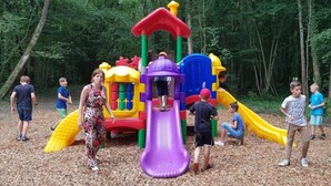 A playground with a slide and climbing structures surrounded by trees.