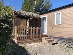 Une maison mobile de plain-pied dotée d’une terrasse en bois, d’une structure de toit en chaume et d’une porte blanche.