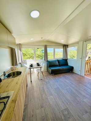 A modern kitchen with a dining area, a sofa, and large windows.