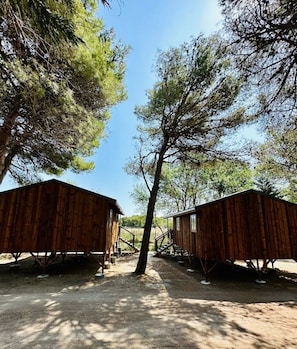 Two wooden cabins with metal supports, surrounded by trees and a clear sky.