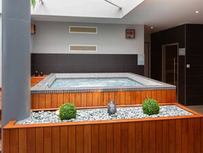 Een wellnessruimte met een whirlpool, houten banken en decoratieve elementen zoals een Boeddhabeeld en plantenbakken.