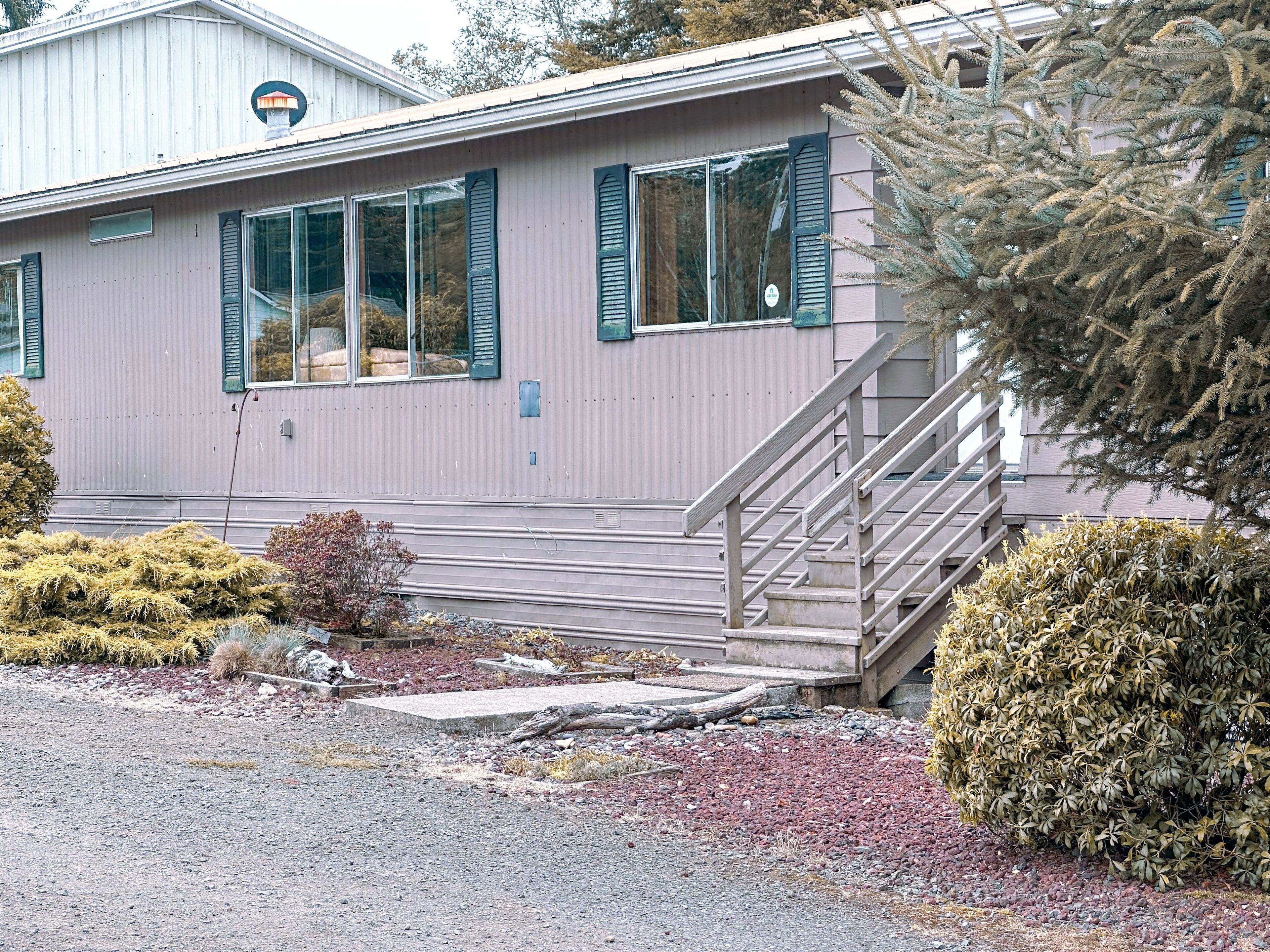 A single-story building with a covered porch, a staircase, and a small garden area with various shrubs.
