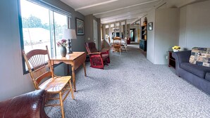 A spacious living room with a high ceiling, a dining area with wooden furniture, and a sofa with a patterned cushion.