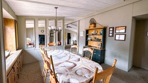 A dining area with a large round table, wooden chairs, a chandelier, and a bookshelf with nautical decorations.