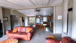 A spacious living room with a leather sofa, a wooden coffee table, and a dining area with a table and chairs. A kitchen is visible in the background.