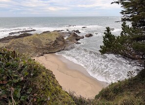 A coastal landscape with rocky outcrops, a sandy beach, and dense greenery.