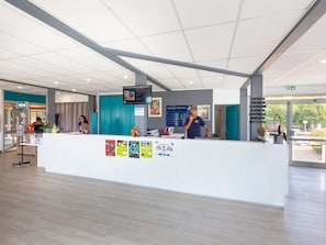 Een moderne receptiebalie met een wit aanrecht, een digitaal scherm en een kalender aan de muur.