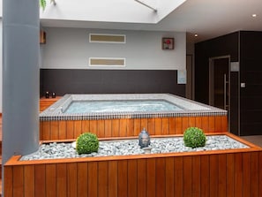 Uma área de spa com hidromassagem, bancos de madeira e elementos decorativos como uma estátua de Buda e plantas em vasos.