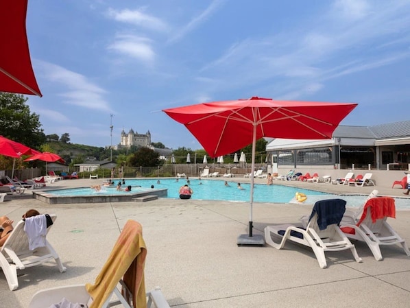 Ein Poolbereich mit mehreren roten Sonnenschirmen, Liegestühlen und einer Burg im Hintergrund.