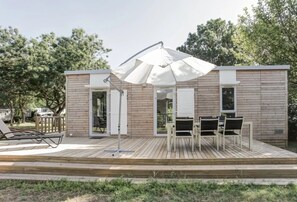 A wooden deck with a table and chairs, a white umbrella, and a door leading to a covered area.
